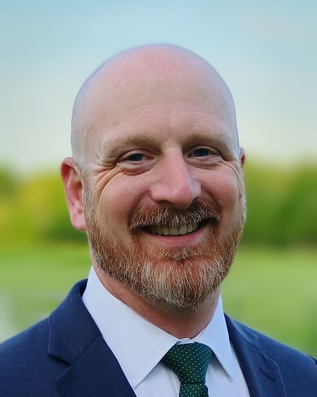 Portrait of Eric Rose, smiling, in a navy suit and green tie